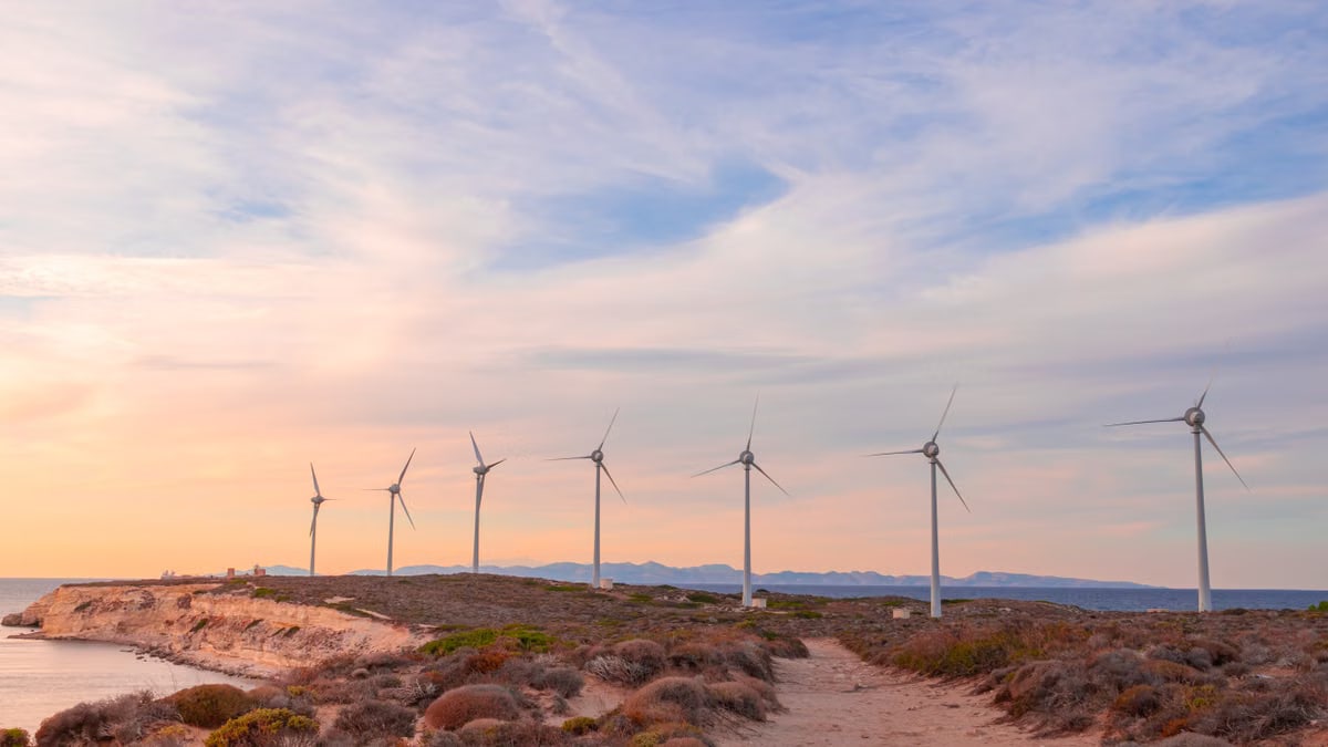 Scenic view of wind turbines along a coastal landscape at sunset, promoting renewable energy.